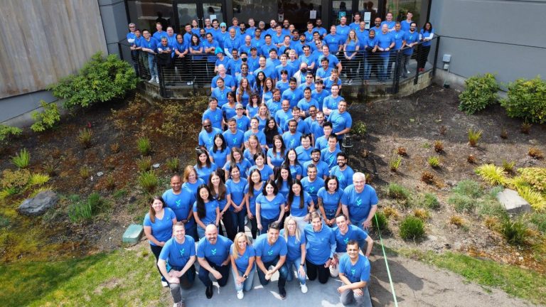Large group of people wearing matching shirts standing outdoors in rows for a team group photo.
