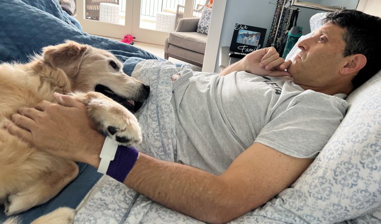 Person lying in bed gently holding a dog close, with the dog resting its head on the person’s body.