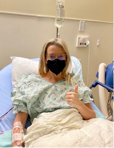 Deb Nielsen sitting up in a hospital bed, wearing a gown and mask.